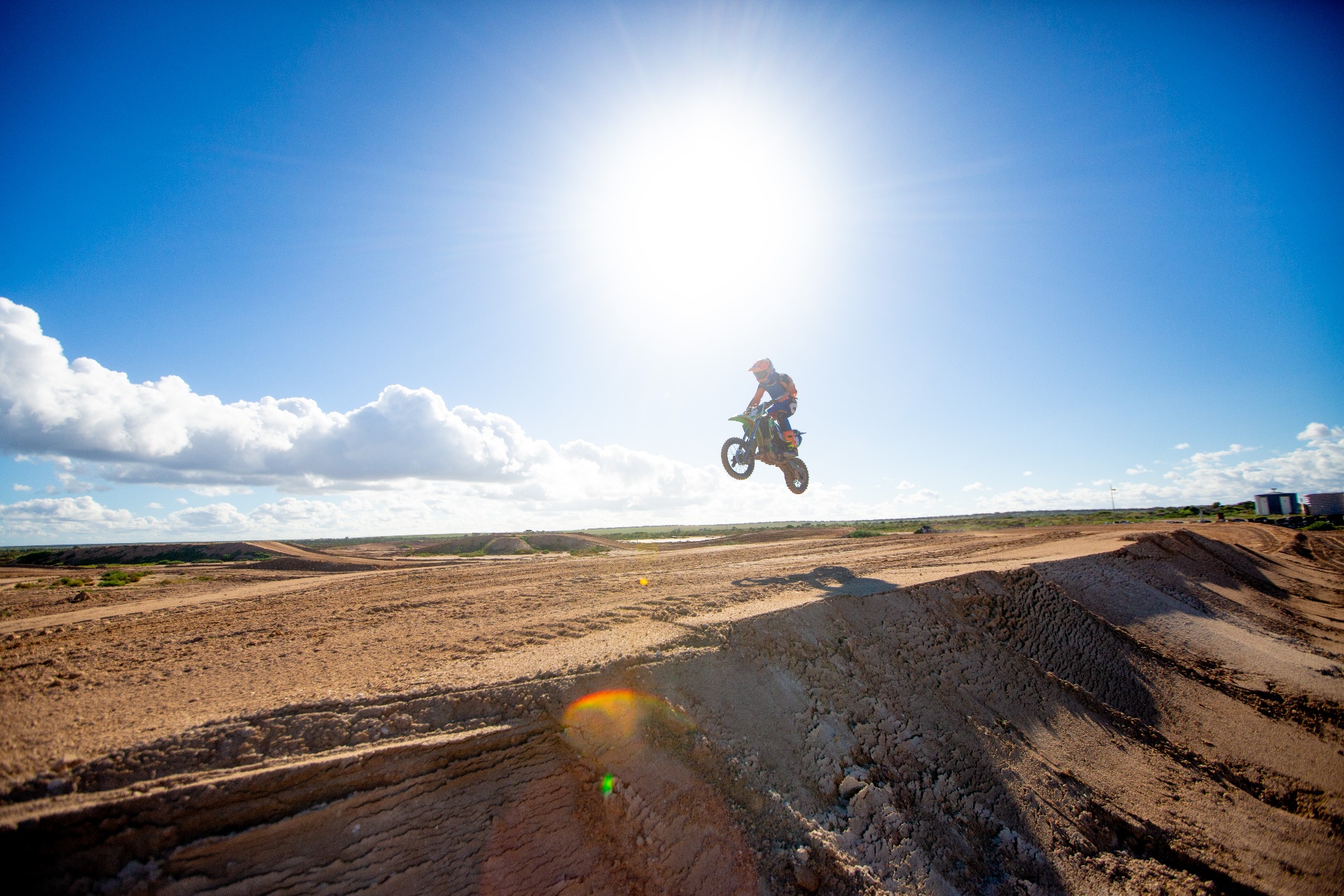 Young rider catching big air on a dirt bike against a bright blue sky